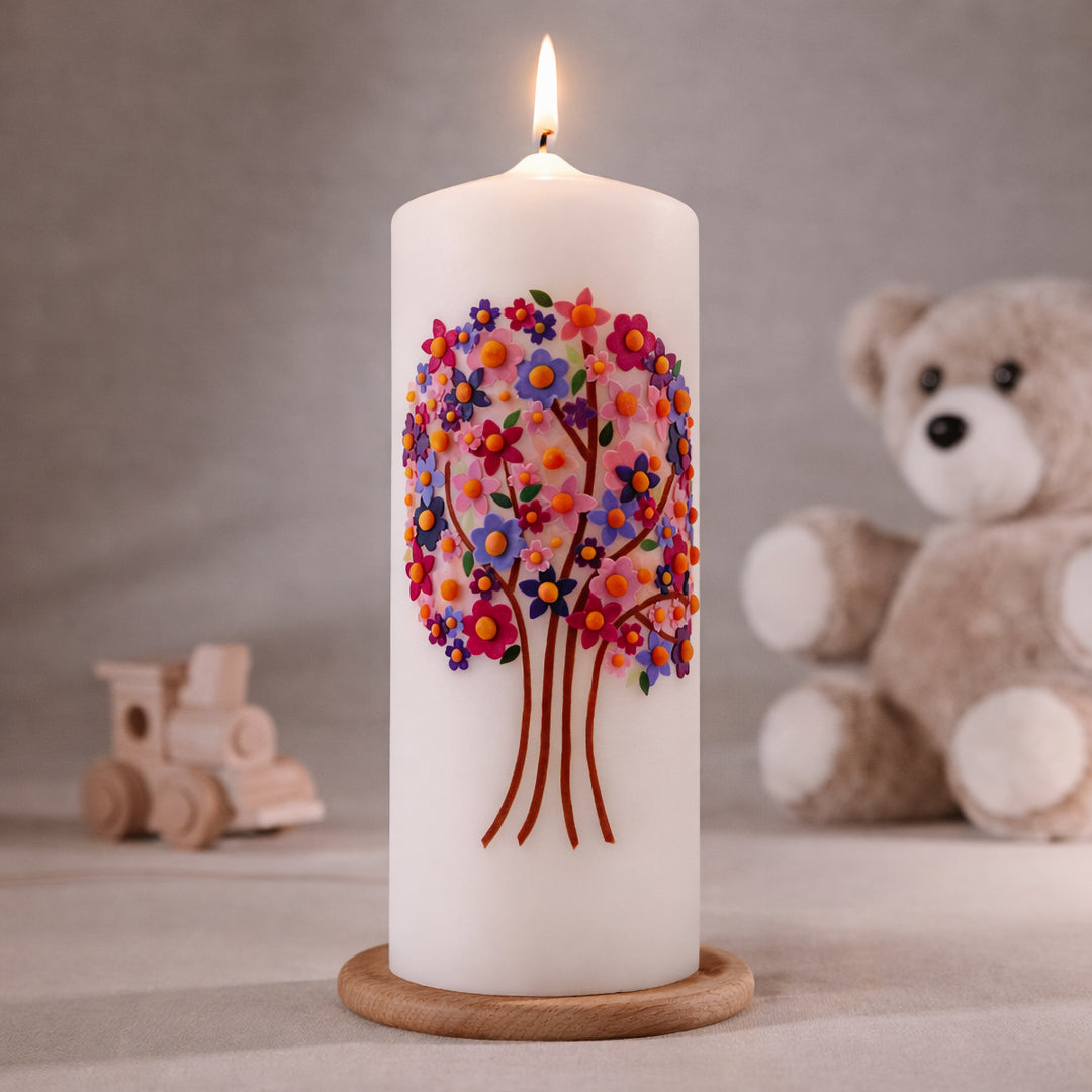 Weiße Taufkerze mit buntem Lebensbaum aus farbigen Blüten und roten Baumstämmen, brennend auf Holzsockel vor neutralem Hintergrund mit Teddybär