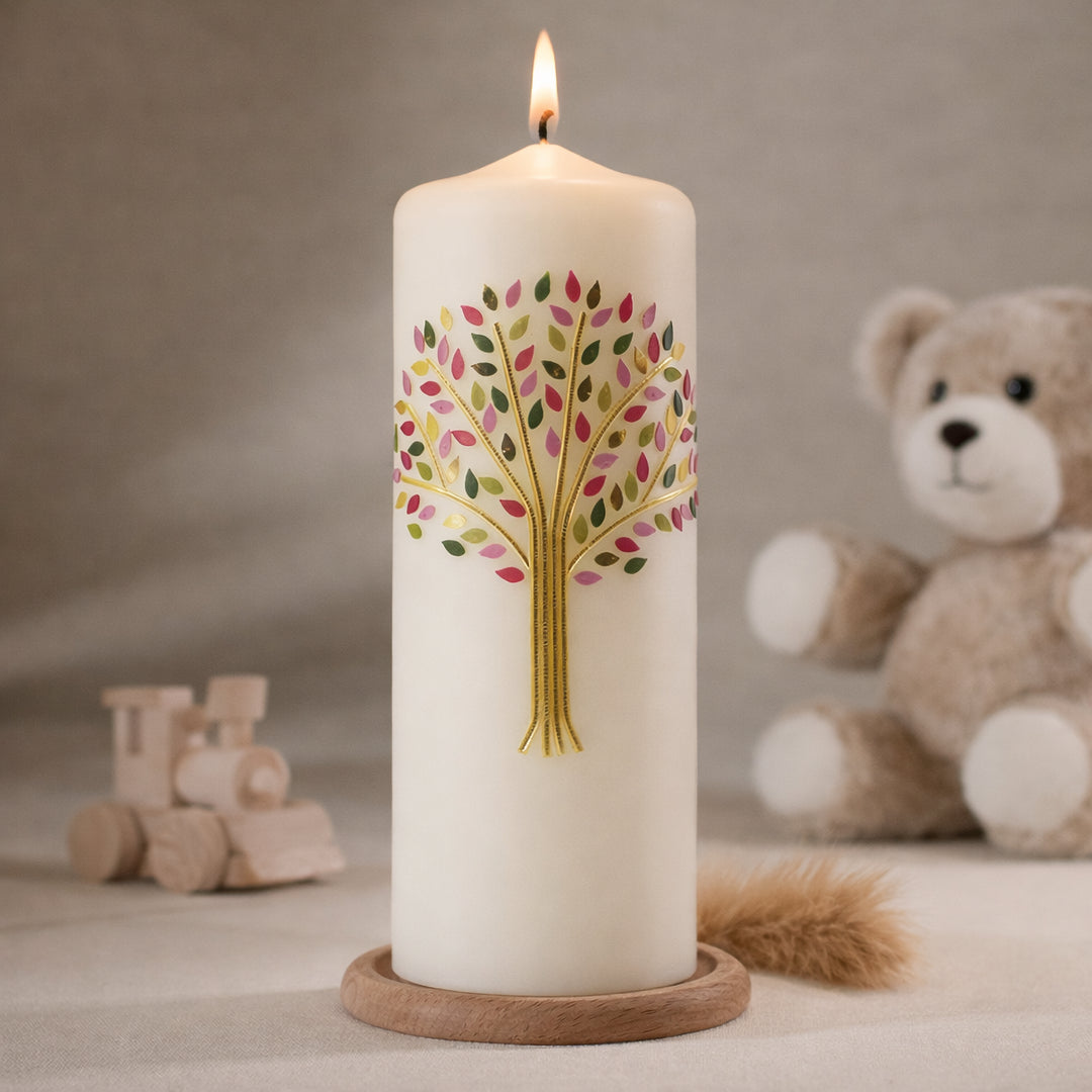 Weiße Taufkerze mit buntem Lebensbaum in Rosa- und Pinktönen, gold stehend auf Holzsockel vor neutralem Hintergrund mit Teddybär