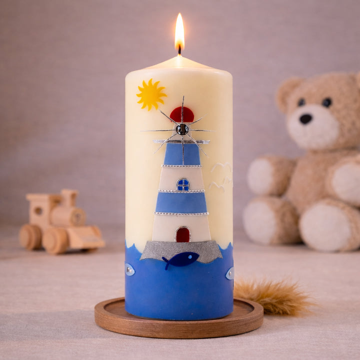 elfenbeinfarbene  Taufkerze mit maritimem Leuchtturm, Sonne und blauem Meer, brennend auf Holzsockel vor neutralem Hintergrund mit Teddybär