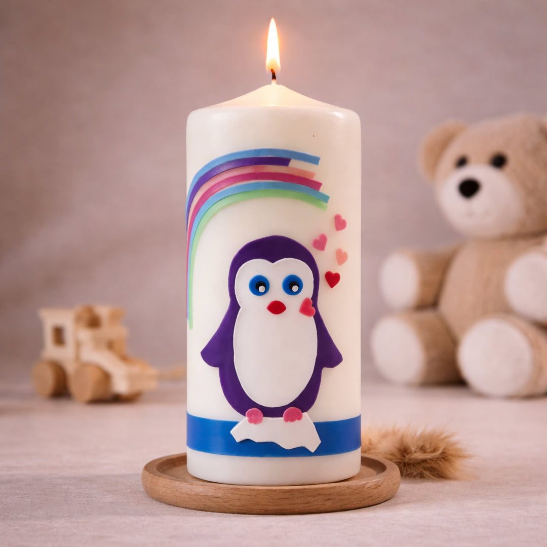 Weiße Taufkerze mit Pinguinmotiv unter buntem Regenbogen und kleinen Herzsymbolen, brennend auf Holzsockel vor neutralem Hintergrund mit Teddybär
