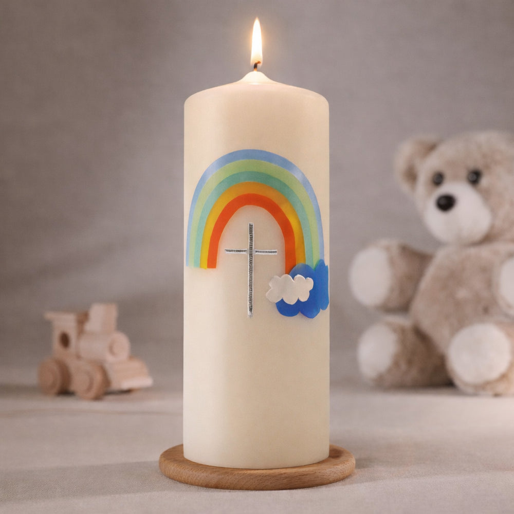 Cremefarbene Taufkerze mit buntem Regenbogen und Wolkenmotiv, brennend auf Holzsockel vor neutralem Hintergrund mit Teddybär