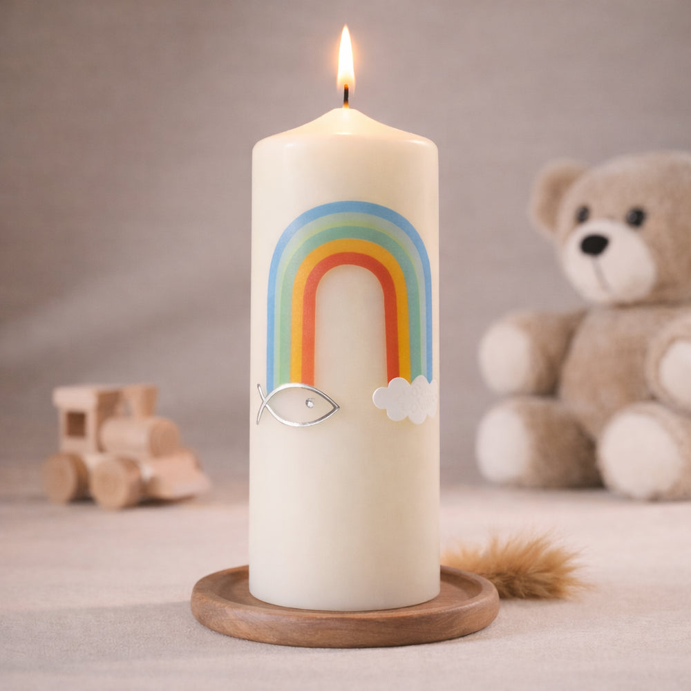 Elfenbeinfarbige Taufkerze mit Regenbogen, christlichem Ichthys-Fischsymbol und Wolken, stehend auf Holzsockel vor neutralem Hintergrund mit Teddybär
