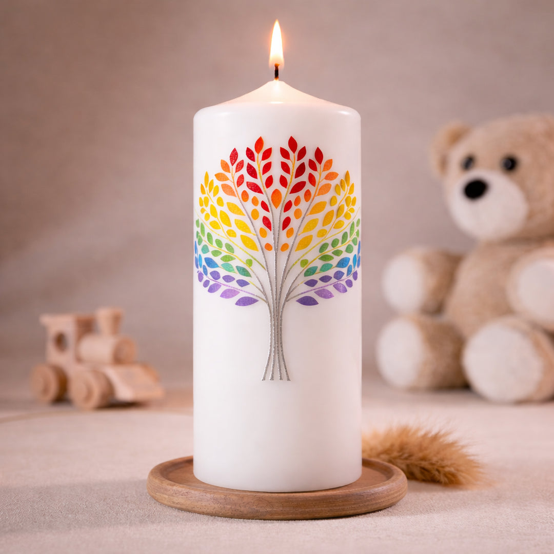 Weiße Taufkerze mit buntem Lebensbaum in Regenbogenfarben, brennend auf Holzsockel vor neutralem Hintergrund mit Teddybär