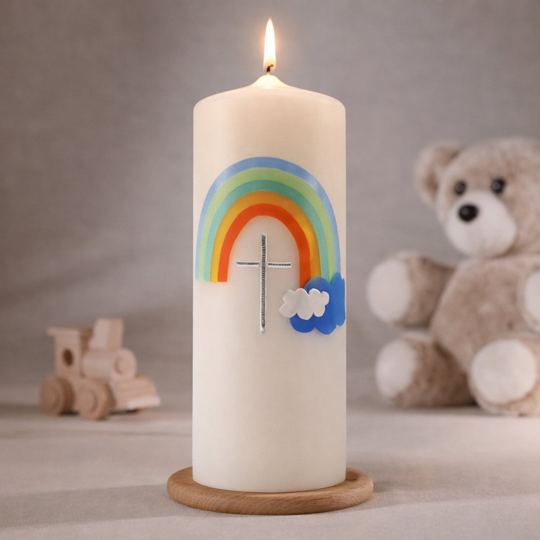 weiße Taufkerze mit buntem Regenbogen und Wolkenmotiv, brennend auf Holzsockel vor neutralem Hintergrund mit Teddybär