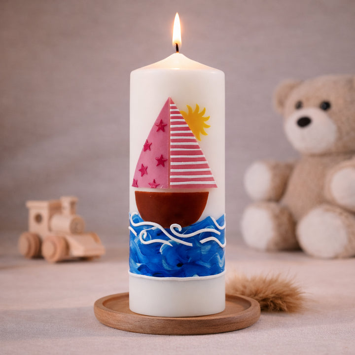 Weiße Taufkerze mit rosa Segelboot, Sonne und blauen Wellen, brennend auf Holzsockel vor neutralem Hintergrund mit Teddybär
