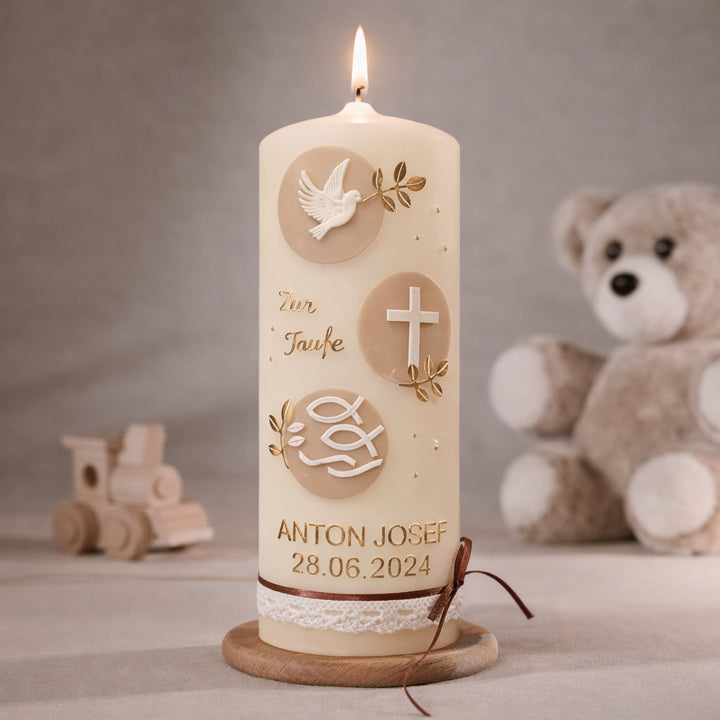 Cremefarbene Taufkerze mit runden Zierelementen in Gold und Beige, Taube, Kreuz und Fischsymbol sowie personalisiertem Namen und Datum, brennend auf Holzsockel vor neutralem Hintergrund mit Teddybär