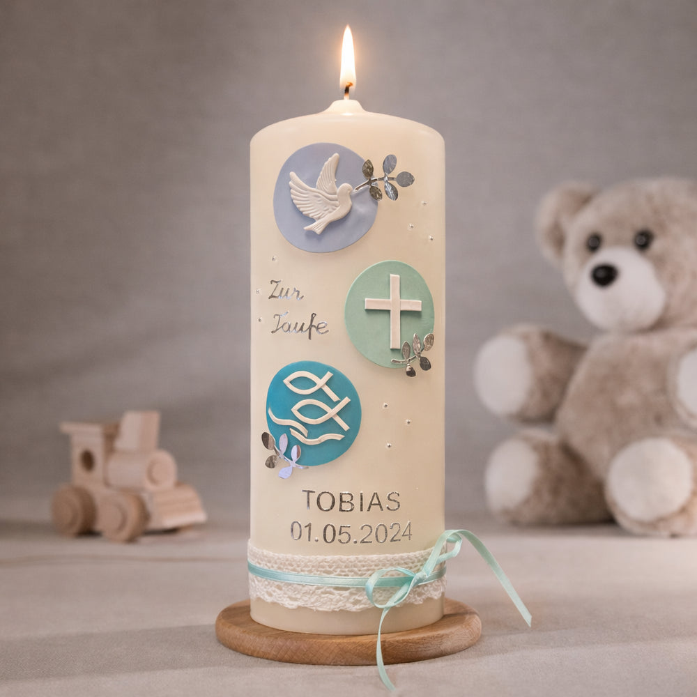 Cremefarbene Taufkerze mit runden Zierelementen in Mint und Blau, Taube, Kreuz und Fischsymbol sowie personalisiertem Namen und Datum, brennend auf Holzsockel vor neutralem Hintergrund mit Teddybär
