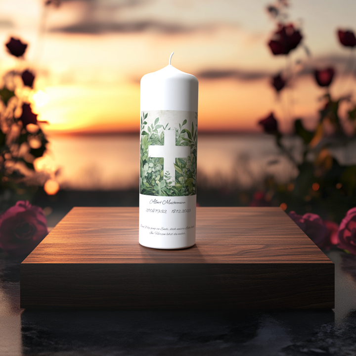 Weiße Trauerkerze mit grünem Blattwerk und weißem Kreuz, auf Holzpodest vor Sonnenuntergang mit Rosen, Symbol für Frieden und Erinnerung.