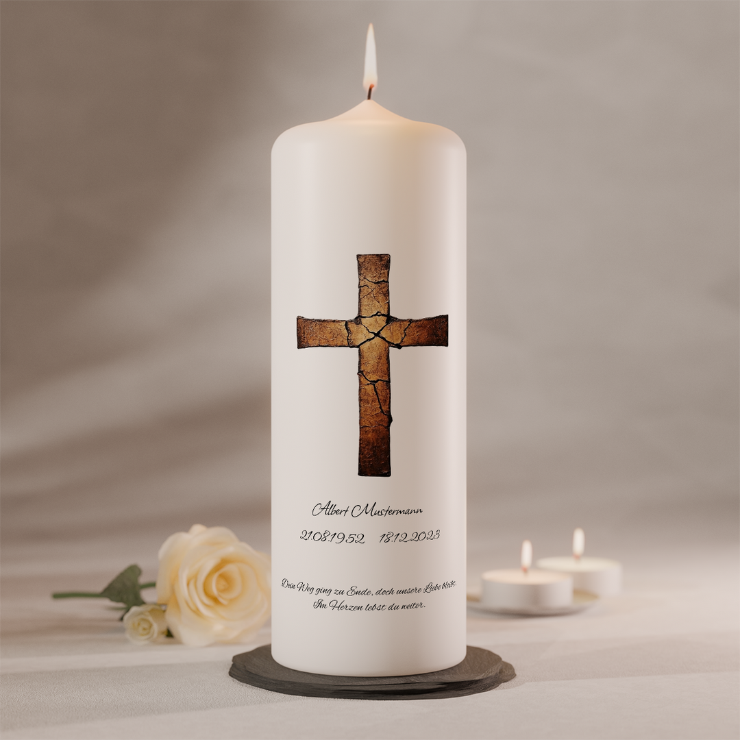 Weiße Trauerkerze mit gebrochenem Kreuz in Kupferoptik und Namensbeschriftung, stehend auf dunklem Kerzenteller neben weißer Rose und zwei Teelichtern