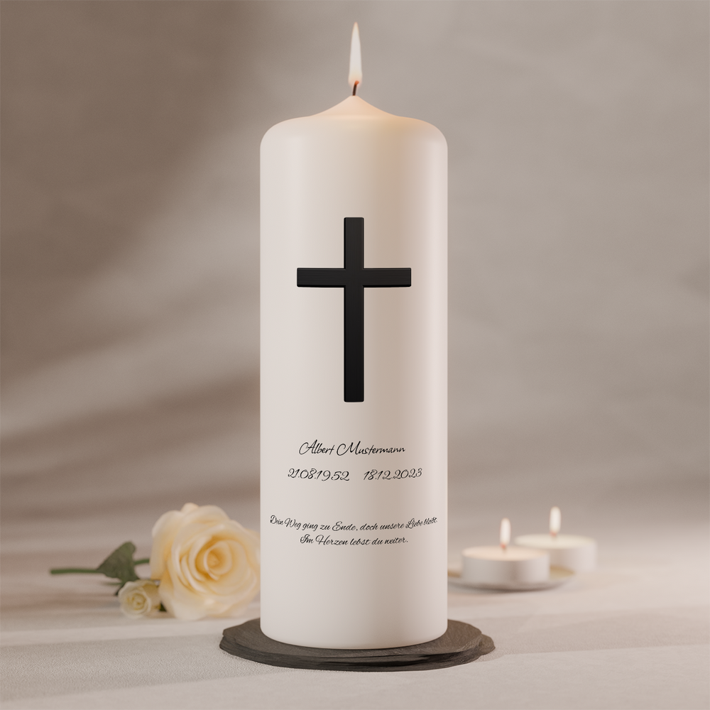 Weiße Trauerkerze mit schwarzem Kreuz und Namensbeschriftung, brennend auf dunklem Kerzenteller neben weißer Rose und zwei Teelichtern