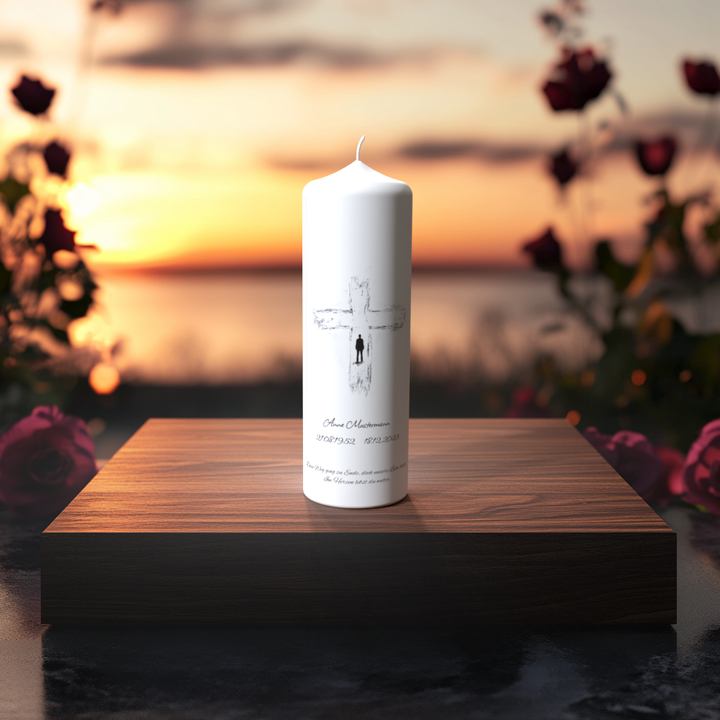 Weiße Trauerkerze mit zartem Kreuz und kleiner Figur – Symbol für Abschied, Licht und Erinnerung bei Sonnenuntergang.