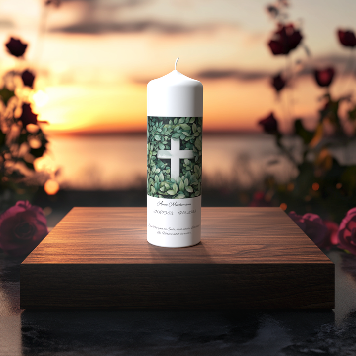 Weiße Trauerkerze mit Kreuz im Blättermotiv auf Holzpodest bei Sonnenuntergang – Symbol für Frieden, Hoffnung und Erinnerung.