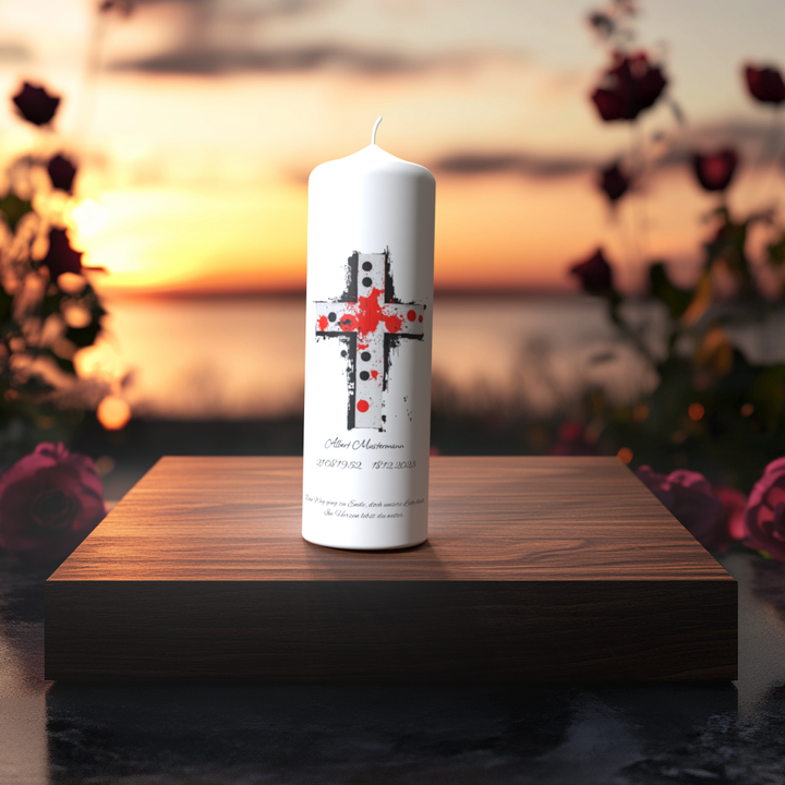 Weiße Trauerkerze mit künstlerischem Kreuz in Rot und Schwarz auf Holzpodest vor Sonnenuntergang – Symbol für Liebe, Schmerz und Hoffnung.