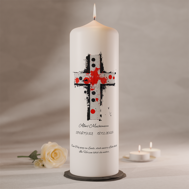 Weiße Trauerkerze mit künstlerischem Kreuz in Rot und Schwarz sowie individueller Beschriftung, stehend auf dunklem Kerzenteller neben weißer Rose und Teelichtern