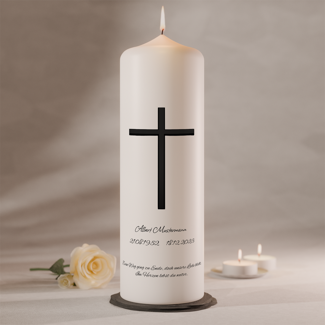 Weiße Trauerkerze mit schlichtem schwarzem Langkreuz und individueller Beschriftung, stehend auf dunklem Kerzenteller neben weißer Rose und Teelichtern

