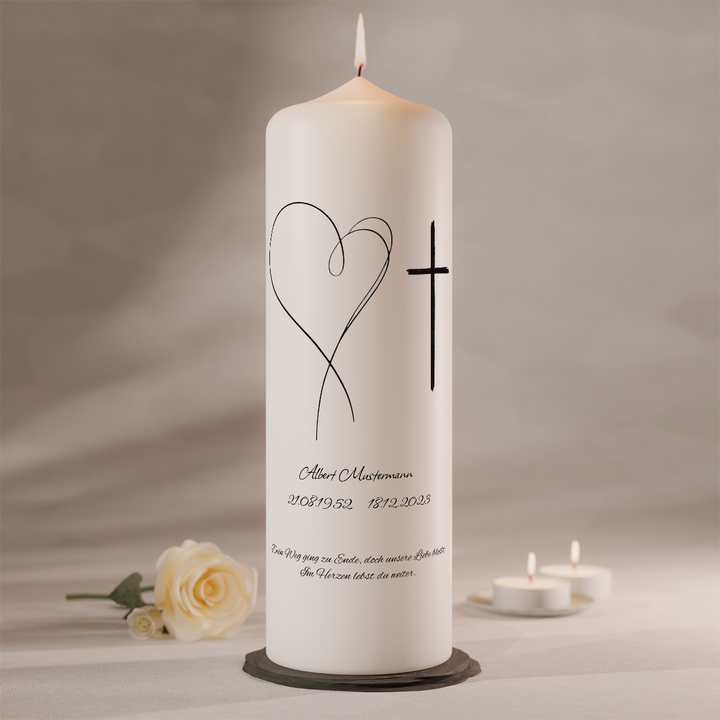 Weiße Trauerkerze mit filigranem Linienherz und schlichtem Kreuz sowie individueller Beschriftung, stehend auf dunklem Kerzenteller neben weißer Rose und Teelichtern