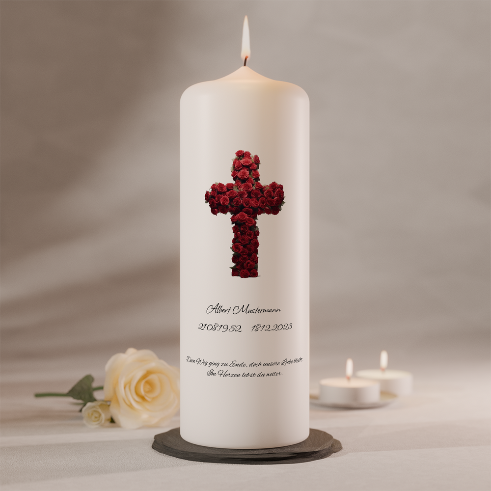 Weiße Trauerkerze mit rotem Rosenkreuz und Namensbeschriftung, brennend auf dunklem Kerzenteller neben weißer Rose und zwei Teelichtern