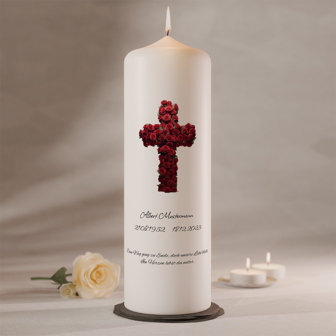 Weiße Trauerkerze mit rotem Rosenkreuz und individueller Beschriftung, stehend auf dunklem Kerzenteller neben weißer Rose und Teelichtern