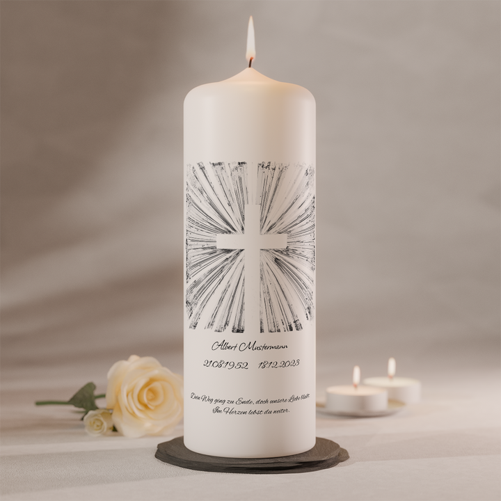 Weiße Trauerkerze mit silbernem Strahlenkreuz und individueller Namensbeschriftung, brennend auf dunklem Kerzenteller neben weißer Rose und zwei Teelichtern