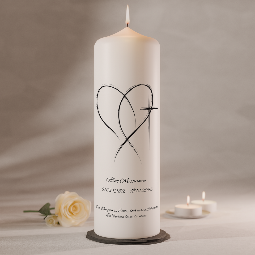 Weiße Trauerkerze mit filigranem Linienherz und Kreuzsymbol sowie individueller Beschriftung, stehend auf dunklem Kerzenteller neben weißer Rose und Teelichtern