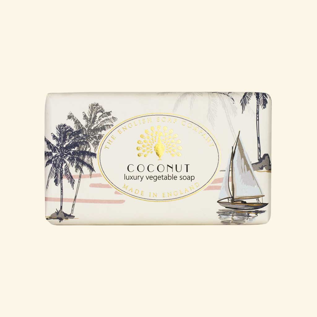 Helle Seife mit tropischer Strandillustration, Palmen und Segelboot, Aufschrift „Coconut – luxury vegetable soap“.