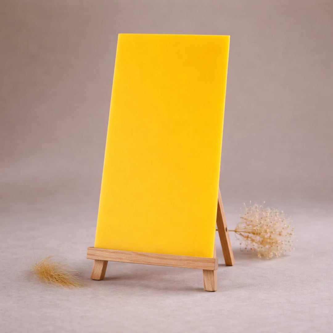 gelbe wachsplatte zur kerzengestaltung auf holzstaffelei vor beigem hintergrund
