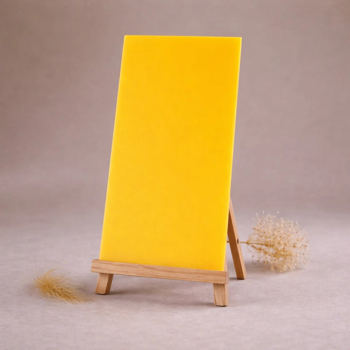 gelbe wachsplatte zur kerzengestaltung auf holzstaffelei vor beigem hintergrund