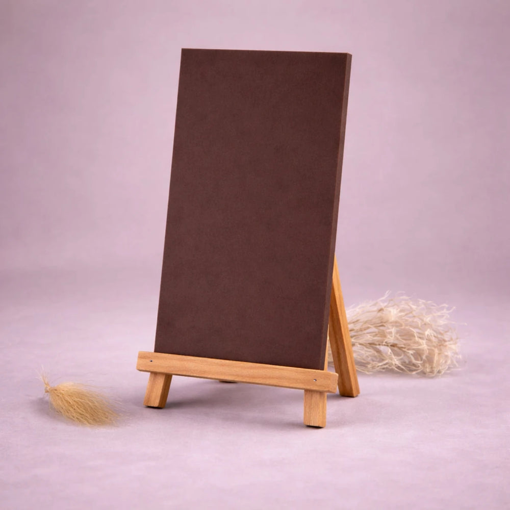 schokobraune wachsplatte zur kerzengestaltung auf kleiner holzstaffelei vor neutralem beigem hintergrund