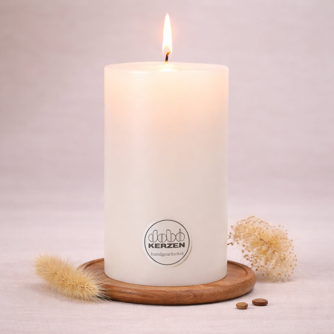 Weiße Stumpenkerze handgefertigt von DOBO mit brennender Flamme auf Holzuntersetzer